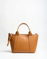 Cartera tipo tote de símil cuero color habano, con asas de mano fijas, detalles de tiras verticales decorativas y correa ajustable removible. Cuenta con el logo metálico de la marca en el frente.