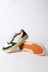 Championes urbanos Urban Haus modelo Mauro, con diseño de paneles en cuero blanco y gamuza verde oliva. Presentan suela de plataforma de goma en tono beige, cierre con cordones blancos y logo de la marca grabado en el lateral.