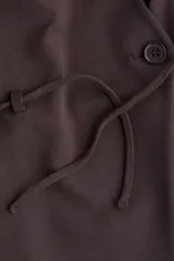 Blazer de punto roma color marrón oscuro, con escote en V profundo, un solo botón de cierre frontal y un cinturón fino para anudar a la cintura.