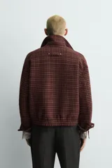 Cazadora de corte relajado confeccionada en tejido con mezcla de lana. Presenta un diseño a cuadros en tonos bordó y marrón, cuello solapa, cierre frontal con cremallera y bolsillos de vivo en la cadera.