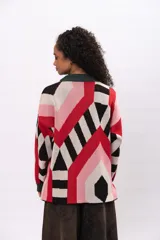 Buzo de tejido de punto con diseño geométrico multicolor en tonos rojo, rosa, negro y beige. Presenta cuello redondo y puños en color verde oscuro.