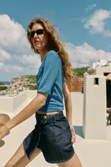 Falda pantalón cruzada de denim en color celeste, con diseño cruzado al frente, cierre frontal oculto y hebilla decorativa redonda en la cintura.