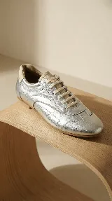 Zapato de cuero plateado con diseño minimalista, cordones al tono y suela plana flexible. Combina la comodidad de un champión con la estética de un zapato formal.