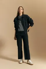 Jean de corte recto y tiro medio, confeccionado en denim elastizado de color negro. Presenta un diseño clásico con cierre de botón y cremallera, bolsillos laterales y traseros, y ruedo con terminación deshilachada.