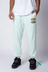 Pantalón de jogging oversize de tela rústica color verde menta, con puños ajustados en los tobillos y un estampado localizado en la parte superior del muslo derecho con las palabras "FUTURE" y "VGP" en tonos naranjas y verdes.