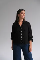Blusa negra de manga larga con cierre frontal de botones, cuello mao y textura sutilmente rayada con detalles bordados.