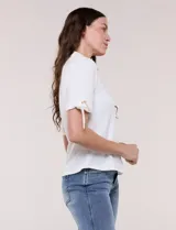 Camisa blanca de manga corta con cuello solapa, cierre frontal de botones, detalles bordados al tono en el pecho y lazos para anudar en las mangas.