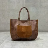 Cartera tipo tote de cuero marrón con textura granulada, presenta detalles de costuras decorativas en los bordes y en la base de las asas.