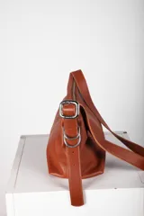 Bandolera Aliada de cuero gris oscuro, con diseño descontracturado, cierre metálico, bolsillo interior y correa ancha regulable con hebilla y argollas metálicas.