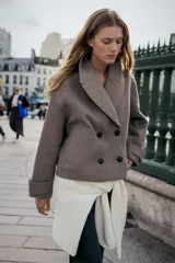 Abrigo corto de paño en color marrón chocolate, con cuello de solapa, cierre frontal cruzado con botones y mangas largas con detalle de trabilla y botón en los puños.