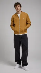 Campera bomber tostada con cierre frontal metálico, bolsillos laterales ribeteados y elásticos en cuello, puños y ruedo. Presenta un pequeño bordado blanco en el pecho.