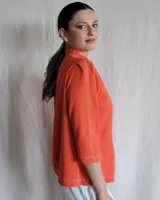 Camisa de manga tres cuartos color beige con cuello con volados y botones frontales. Presenta un detalle de color negro en la parte superior de las mangas.