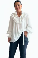 Blusa blanca de estilo romántico con volados tipo shabot en el frente, cuello alto con lazo ajustable y mangas largas abullonadas con puños ajustados.