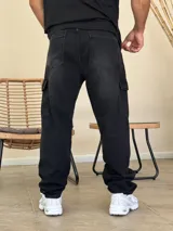 Pantalón tipo cargo de denim color negro con efecto lavado. Presenta corte holgado, bolsillos laterales con solapa y costuras reforzadas en las rodillas.