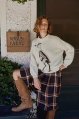 Sweater de lana color crudo con cuello redondo tejido y estampa frontal de un tero. Presenta un diseño de corte holgado con puños y ruedo acanalados.