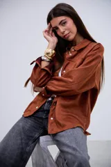 Sobrecamisa de gamuza color terracota, con cuello clásico, cierre frontal de botones metálicos, bolsillos en el pecho y mangas largas con puños abotonados.