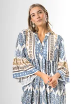 Maxi vestido largo de fibrana en color blanco con estampado paisley y geométrico en tonos azules y tostados, con escote en V, mangas largas amplias y diseño holgado con volados en la falda.