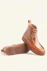 Bota de cuero vacuno color bordó con acabado charol, diseño de caña media con cordones y ganchos metálicos. Presenta costuras visibles en la puntera y suela de goma tipo crepe.