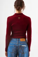 Top de tejido de punto acanalado color bordó, de manga larga y cuello polo con botones frontales.