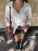 Camisa de corte oversize con estampado de rayas verticales finas en tonos blanco y gris. Presenta cuello clásico, cierre frontal con botones y mangas largas con puños abotonados.