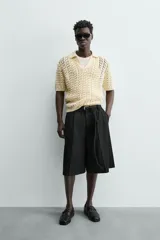 Polo de punto con estructura calada en color beige, confeccionado en algodón. Presenta un calce relajado, manga corta, cuello solapa con abertura frontal y terminaciones acanaladas.