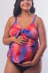 Tankini maternal con estampado degradado en tonos rojos, naranjas y azules. Presenta un nudo decorativo en el centro del escote, breteles regulables y un diseño holgado diseñado para adaptarse al embarazo.
