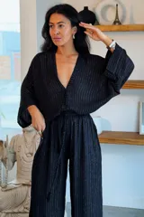 Conjunto de camisa y pantalón de viscosa negro con finas líneas metalizadas doradas. La camisa es de manga larga con escote en V y botones frontales, mientras que el pantalón es de corte ancho y tiro alto con cintura elástica fruncida.