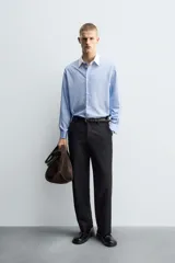 Camisa de corte regular fit confeccionada en algodón, con estampado de rayas verticales en tonos azul y blanco. Presenta cuello italiano en color blanco a contraste, cierre frontal de botones y mangas largas con puños dobles.
