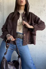 Chaqueta de gamuza color chocolate, con corte recto, cuello clásico y cierre frontal con botones. Presenta un diseño calado decorativo en el ruedo y bolsillos frontales tipo parche.