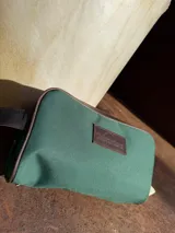 Necessaire de lona color verde con detalles en cuero marrón, incluyendo una etiqueta con el logo "Sierra Mora".