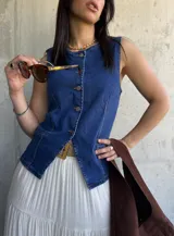 Chaleco de denim azul con escote en V y cierre frontal con botones. Tiene dos bolsillos frontales a la altura de la cintura.