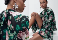Blusa de gasa con estampado floral en tonos rosa, verde y negro. Tiene cuello alto, mangas largas con volantes y cierre de lazo en la parte posterior.