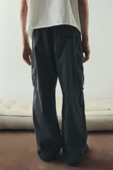 Pantalón cargo de algodón, color negro lavado, con corte holgado y cordón ajustable en cintura y tobillos. Presenta bolsillos cargo grandes en las piernas con solapas y pliegues cosidos en las rodillas.