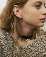 Gargantilla tipo choker de gamuza con dijes colgantes artesanales de metal y perlas naturales. Cuenta con tiras largas para atar y ajustar en la parte posterior.