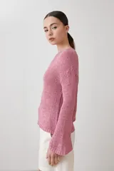 Sweater de punto fino en color verde, con cuello redondo y mangas largas. Presenta un detalle integrado de pañuelo estampado con motivos florales en la parte inferior, que se cruza sobre la cintura.