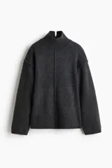 Buzo oversized de punto suave, color gris oscuro, con cuello alto acanalado y abertura trasera en V. Presenta costuras decorativas verticales y hombros caídos con mangas largas.