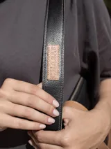 Cartera negra de cuero genuino con correa corta de cuero color tostado y correa larga de cinta negra con letras blancas.