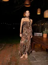 Vestido largo estampado en tonos tierra, con cuerpo fruncido estilo strapless y un pañuelo anudado al cuello. La falda presenta tajo y volados asimétricos.