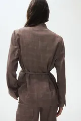 Blazer de corte recto con estampado a cuadros, escote en pico sin solapas y frente superpuesto. Presenta hombreras, bolsillos delanteros ribeteados, aberturas en los puños y un cinturón fino extraíble con anillas en D para ajustar en la cintura.
