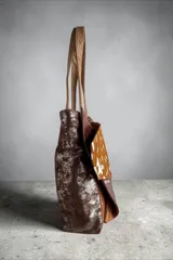 Cartera tipo shopper confeccionada en cuero con diseño patchwork en tonos marrones y animal print, asas de hombro en tono tostado y detalle de dije colgante metálico triangular.