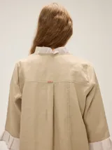 Camisa de lino de silueta relajada y largo irregular, color beige, con cuello mao, botones frontales a contratono y mangas tres cuartos terminadas en volados.