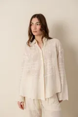 Camisa de manga larga color crema, confeccionada en algodón con bordados florales. Presenta cuello clásico, cierre frontal con botones y corte holgado.