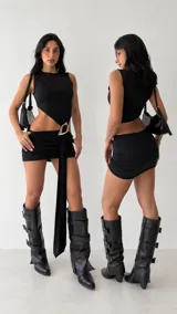 Vestido corto negro con diseño asimétrico, abertura cut-out en la cintura, tiras drapeadas con hebilla metálica decorativa y falda tubo ajustada.