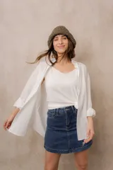 Camisa blanca de calce amplio, confeccionada en tejido liviano con sutiles rayas verticales, cuello clásico, mangas largas con hombros caídos y abotonadura frontal.