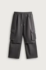Pantalón jogger de corte relajado confeccionado en tejido de algodón compacto con elasticidad. Presenta cintura elástica ajustable con cordón, bolsillos laterales, bolsillos cargo con solapa en las piernas y detalle de pliegues en las rodillas.