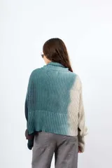 Saco de hilo con cuello alto y cierre de botones, de tejido de punto y diseño oversize. Presenta un teñido artesanal degradado que combina gris y beige, con mangas largas y puños amplios, además de un detalle de aplicación floral oscura en el pecho.