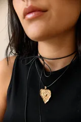 Collar con dije de corazón en acero quirúrgico, con textura irregular y relieve, montado sobre un tiento encerado negro.