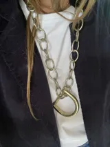 Collar de cadena gruesa de eslabones grandes en color dorado, con un dije central en forma de estribo de montar.