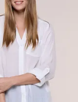 Blusa de calce relajado color salmón, confeccionada en tela liviana con textura sutil. Presenta escote en V con abotonadura frontal, bolsillo parche en el pecho, mangas largas regulables con presilla y ruedo con opción de anudar en el frente.