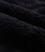 Buzo de tejido peludo color negro, con cuello alto y cierre frontal parcial. Presenta mangas largas con puños elásticos, bolsillo tipo canguro y etiqueta decorativa en el pecho.
